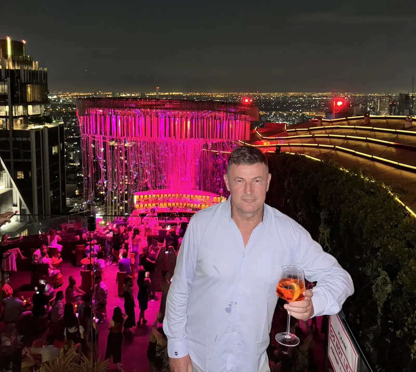 Blaise Jaeger avec un cocktail au rooftop Tichuca sous son installation lumineuse rose, Bangkok