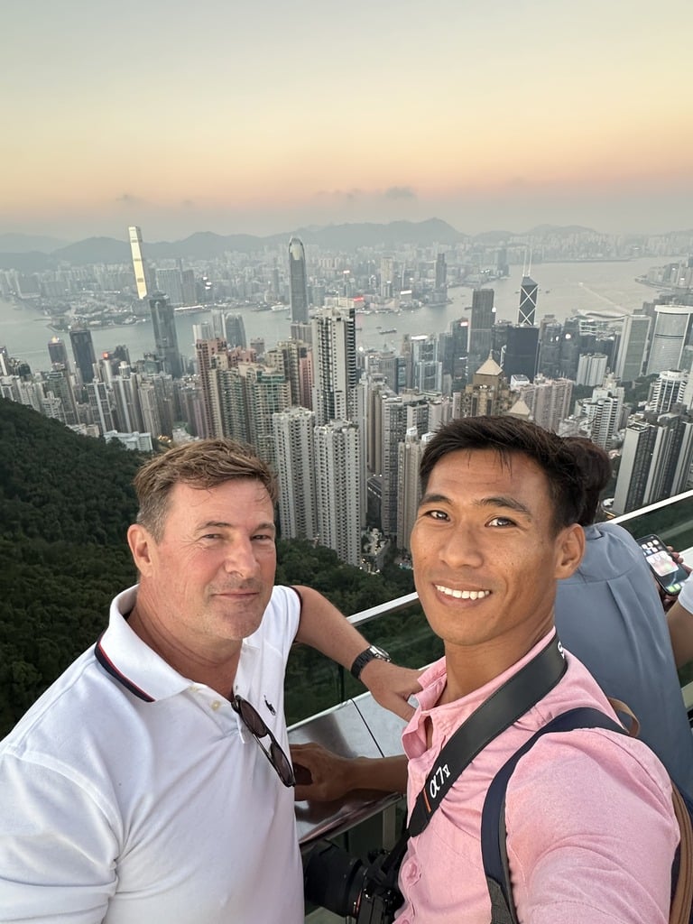 Blaise Jaeger et Roy en selfie au Victoria Peak au coucher du soleil avec les gratte-ciel de Hong Kong derrière eux