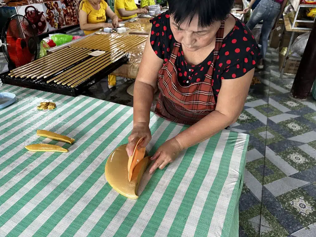 Une femme découpe des bonbons à la noix de coco à la main dans un atelier de Ben Tre, delta du Mékong