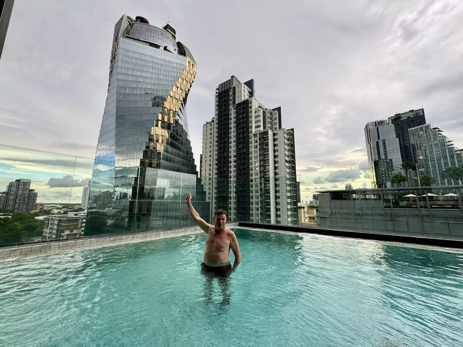 Blaise Jaeger dans la piscine sur le toit de l'Ascott Thonglor face à une tour de verre torsadée, Bangkok