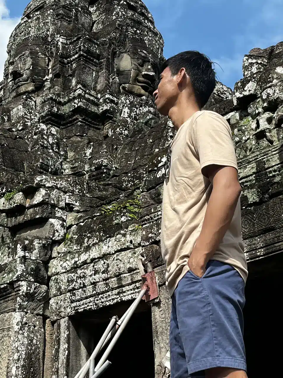 Roy à côté d’une tour à visages de pierre du Bayon, à Angkor Thom